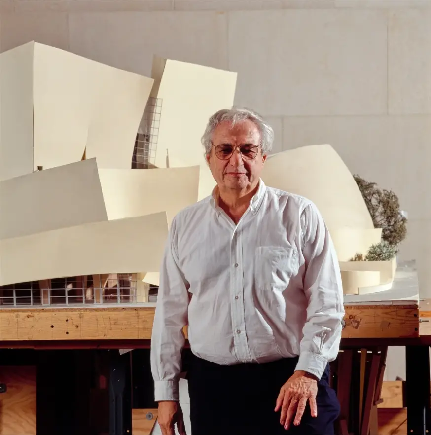 Frank Gehry stands in front of a large model of Walt Disney Concert Hall.