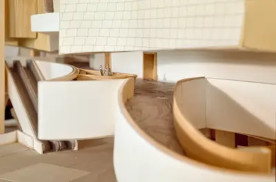 A scale model of the interior of the Walt Disney Concert Hall lobby constructed in foam board and wood shows ramps, balconies, and walls. A printed pattern on the floor suggests a carpet with an abstract floral motif.