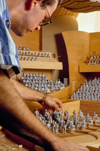 A person adjusts a figurine within a scale model of the Walt Disney Concert Hall interior