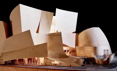 An eye-level view of a model of Walt Disney Concert Hall constructed in textured beige paper, acrylic, and wood is dramatically lit from within, suggesting the dynamic appearance of the building at night.