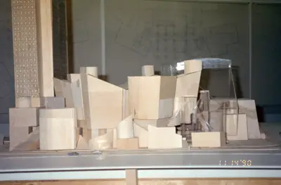 An eye-level view of a model of Walt Disney Concert Hall constructed in wood and acrylic suggests the appearance of a building composed of stacked wooden blocks. Drawings and other office ephemera are visible in the background.