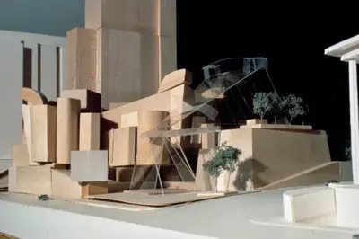 An eye-level view of a model of Walt Disney Concert Hall constructed in wood and acrylic suggests the appearance of a building composed of vertically oriented wooden blocks. Scale cars and trees afford realism.
