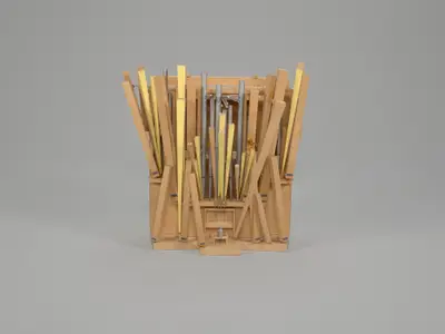 A scale model of an organ constructed in wood with pipes positioned at dynamic angles. Some pipes are painted to suggest the appearance of metal, others are colored yellow. A small figurine sits at the organ as if playing, suggesting the large scale of the instrument.