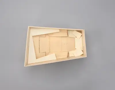 A model of the Walt Disney Concert Hall interior constructed in simple, beige materials schematically illustrates the angular walls of the asymmetrical room and the arrangement of seats, balconies, and the stage within it. Printed lines suggest the placement of aisles, stairs, and other details.