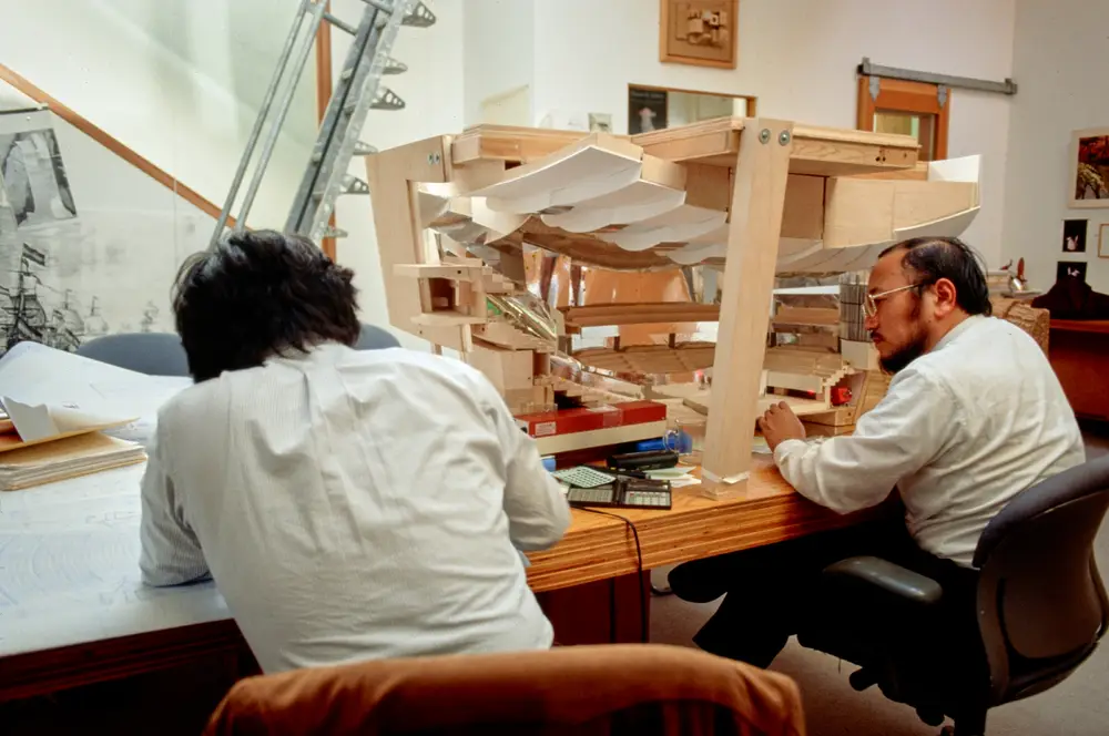 Two people sit in front of a model of Walt Disney Concert Hall, taking measurements by laser.