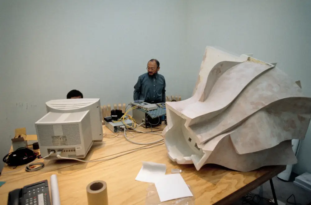 Two people sit in front of a computer, sound devices, and a model of Walt Disney Concert Hall.