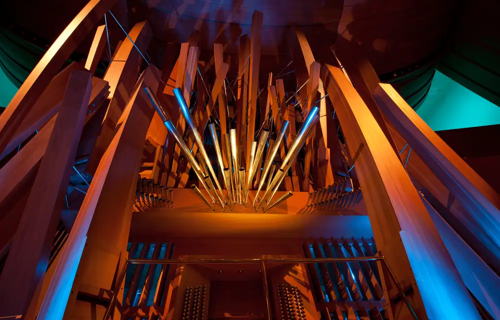 A close-up photograph of the Walt Disney Concert Hall organ, with its pipes in wood and in metal playfully arrayed, awash in bright, colorful lighting.