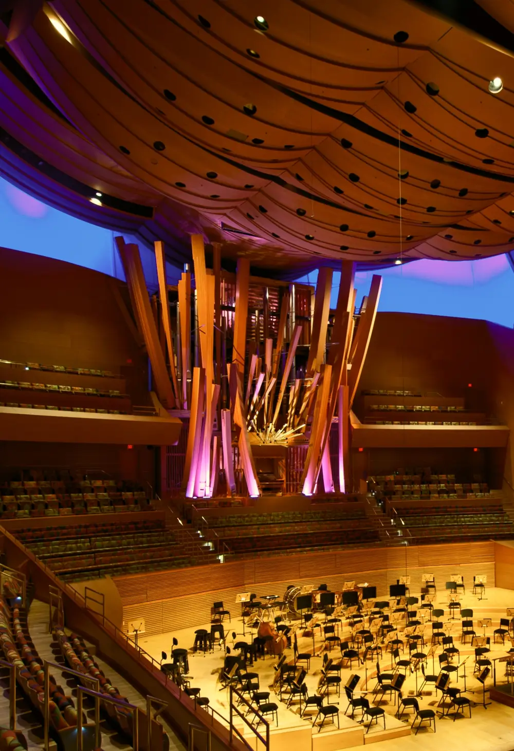 An interior view of Walt Disney Concert Hall from an upper level towards the stage and organ. The hall and seats that surround the stage on all sides are empty, showcasing the sweeping forms and warm colors of the hall's interior architecture.