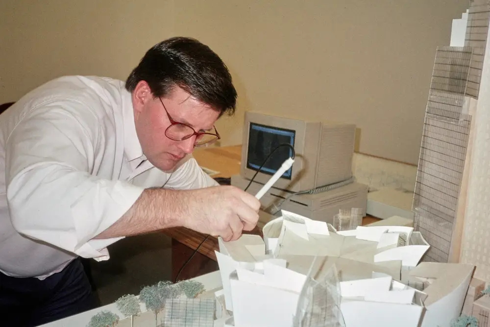 A person traces the profile of a model of Walt Disney Concert Hall with an electronic pen connected by a cord to a computer sitting in the background.
