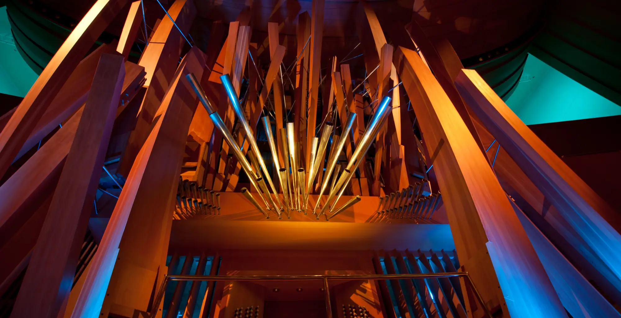 A close-up photograph of the Walt Disney Concert Hall organ, with its pipes in wood and in metal playfully arrayed, awash in bright, colorful lighting