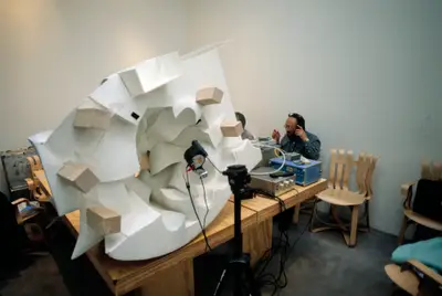 Two people sit in front of a model of Walt Disney Concert Hall. An acoustic measuring device stands in front of the physical model.