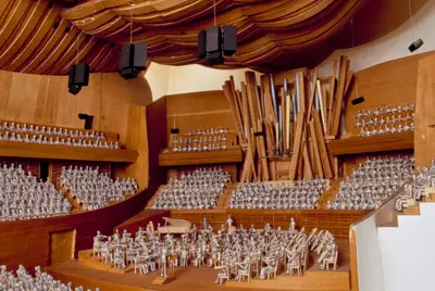 A scale model of an organ with dynamically arrayed pipes sits within a highly detailed scale model of the Walt Disney Concert Hall interior, outfitted with figurines representing concertgoers and performers.