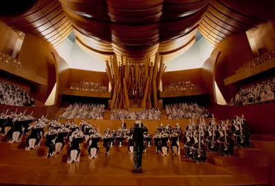 An immersive view of a scale model of the Walt Disney Concert Hall interior shows the stage and organ. Figurines of musicians are arranged on stage, and figurines representing the audience sit in seats surrounding the stage.