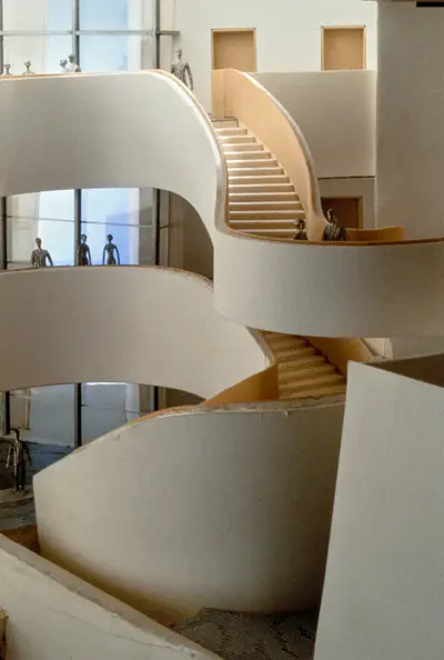 A scale model of the interior of the Walt Disney Concert Hall lobby constructed in foam board and wood shows stairs, balconies, windows, and doors. Scale figurines of concertgoers populate the space.