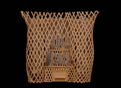 A scale model of an organ constructed in wood with pipes oriented vertically and painted to suggest the appearance of metal. The instrument is surrounded by a wooden latticework obscuring parts of the organ.