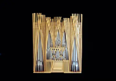A scale model of an organ constructed in wood with pipes oriented vertically and painted to suggest the appearance of metal. The instrument is surrounded by vertical wooden elements which fan out and upward toward the ceiling.