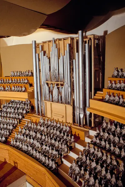 A scale model of an organ constructed in wood with pipes oriented vertically and painted to suggest the appearance of metal. The instrument is placed within a model of the interior of the Walt Disney Concert Hall, with small figurines representing audience members in surrounding seats.