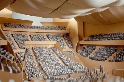 A view into a highly detailed interior model of Walt Disney Concert Hall suggests the appearance of a performance, with audience members in seats and performers on stage represented in two-dimensional photographic cutouts. The wooden interior is awash with what appears to be natural light.
