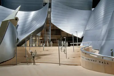 A close-up view of a model of Walt Disney Concert Hall constructed in metal-foil paper, acrylic, and wood highlights the building's entrance, with figurines on its steps suggesting a sense of realism.