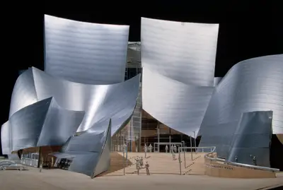 A eye-level view of a model of Walt Disney Concert Hall constructed in metal-foil paper, acrylic, and wood against a black background appears to represent a completed building. Scale cars and figurines reinforce this sense of realism.
