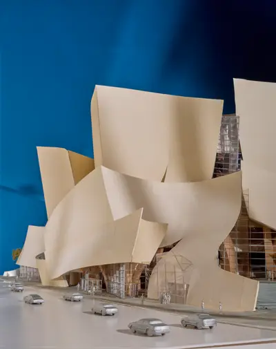 A dramatically lit model of Walt Disney Concert Hall against a blue background highlights the building's curving forms and is populated with figurines and model cars.