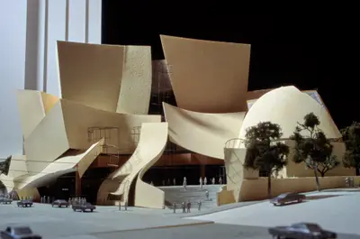 An eye-level view of a model of Walt Disney Concert Hall constructed in textured beige paper and wood suggests the dynamic appearance of the building. Scale cars, trees, and figurines afford realism.