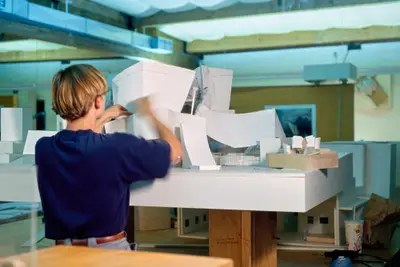 A person in an office constructs a large model of Walt Disney Concert Hall in paper and acrylic.