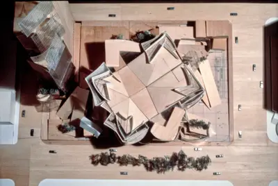 An aerial view of a model of Walt Disney Concert Hall constructed in wood, acrylic, and paper suggests the complex form of the building within its urban context. Scale cars and trees afford realism.