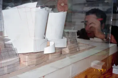 A close-up view of a model of Walt Disney Concert Hall encased in a clear acrylic box. A close-up view shows a person tracing the model's outlines in red ink on the acrylic.