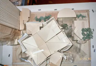 An aerial view of a model of Walt Disney Concert Hall constructed in wood, acrylic, and paper suggests the complex form of the building within its urban context. Scale cars and trees afford realism, while scissors at the edge of the frame suggest that this is still a work in progress.