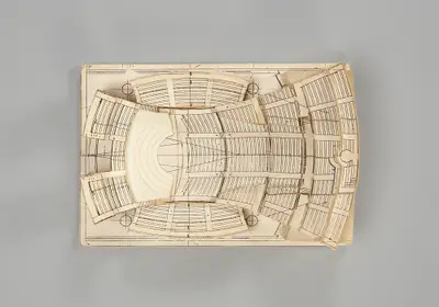 A model of the Walt Disney Concert Hall interior constructed in simple, beige materials schematically illustrates the dimensions of the rectangular room and the arrangement of seats and the stage. Printed lines suggest the placement of aisles, stairs, and other details.