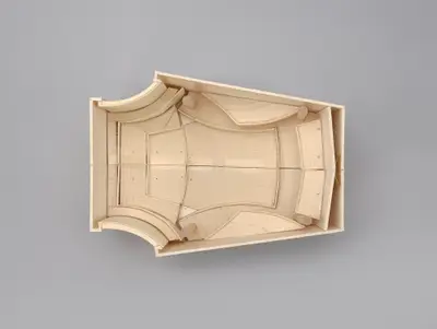 A model of the Walt Disney Concert Hall interior constructed in simple, beige materials schematically illustrates the alternating curved and straight walls of the room and the arrangement of seats, balconies, and the stage within it. Penciled and printed lines suggest the placement of aisles, stairs, and other details.