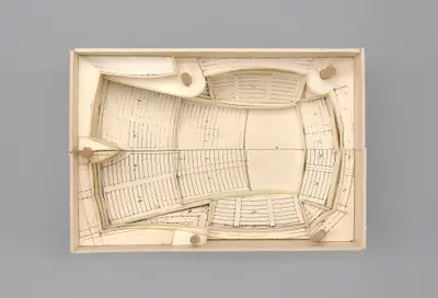 A model of the Walt Disney Concert Hall interior constructed in simple materials schematically illustrates the rectangular dimensions of the room and the arrangement of seats, balconies, and the stage within it. Printed lines suggest the placement of aisles, stairs, and other details.